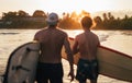 Palm trees lightened with the sunset sun. with father with teenage son walking with surfboards by the sandy ocean Dewata beach in Royalty Free Stock Photo