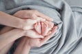 The palms of mom and dad hug the feet of a newborn child on a gray background, parental love and care Royalty Free Stock Photo