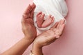 The palms of the mother are holding the foot of the newborn baby in white blanket, pink background. Royalty Free Stock Photo