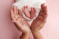 The palms of the mother are holding the foot of the newborn baby in white blanket, pink background. Royalty Free Stock Photo