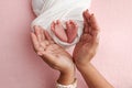 The palms of the mother are holding the foot of the newborn baby in white blanket, pink background. Royalty Free Stock Photo