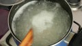 A pan of boiled rice is boiling. The lid is lifted, rice is stir. Lid closes. Boiled rice in a dark blue pan