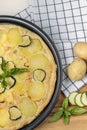 A pan of quiche with basil leaves, potatoes and sliced zucchini on a wooden cutting board with whole potatoes beside it Royalty Free Stock Photo
