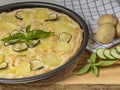 A pan of quiche with potatoes and sliced zucchini on a wooden cutting board with whole potatoes beside it Royalty Free Stock Photo