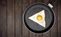 Fried egg with triangle shape on frying pan on wooden background