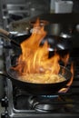Pan on fire while flambeeing prawns for a delectable meal in a commercial kitchen, big skillet in flames