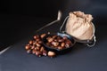 Pan with fried edible chestnuts, jute sack on black table background with sunlight ray. Traditional healthy organic