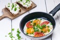 Pan of fried eggs with tomatoes, cheese, spring onion, herbs on a white table. Bread with spread. White wooden table. Concept of f Royalty Free Stock Photo