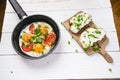 Pan of fried eggs with tomatoes, cheese, spring onion, herbs on a white table. Bread with spread. White wooden table. Concept of f Royalty Free Stock Photo