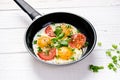 Pan of fried eggs with tomatoes, cheese, spring onion, herbs on a white table. White wooden table. Concept of food. Breakfast time Royalty Free Stock Photo