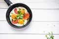 Pan of fried eggs with tomatoes, cheese, spring onion, herbs on a white table. White wooden table. Concept of food. Breakfast time Royalty Free Stock Photo