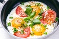 Pan of fried eggs with tomatoes, cheese, spring onion, herbs on a white table. White wooden table. Concept of food. Breakfast time