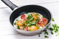 Pan of fried eggs with tomatoes, cheese, spring onion, herbs on a white table. White wooden table. Concept of food. Breakfast time Royalty Free Stock Photo