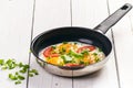 Pan of fried eggs with tomatoes, cheese, spring onion, herbs on a white table. White wooden table. Concept of food. Breakfast time Royalty Free Stock Photo