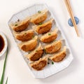 Pan-fried gyoza dumpling jiaozi in a plate with soy sauce on white table background