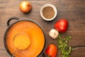 Pan and ladle full of tomato puree soup, ingredients on a wooden background.