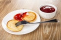 Pancake on fork, pancake poured jam in saucer, bowl with strawberry jam on table