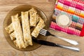 Pancake rolls in plate, piece of pancake on fork, mayonnaise in bowl on napkin, knife on wooden table. Top view Royalty Free Stock Photo