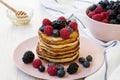 Pancakes with berries and honey on a pink plate over white wooden background, low angle. Royalty Free Stock Photo