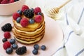 Pancakes with berries and honey on a pink plate over white wooden background, side view. Royalty Free Stock Photo