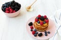 Pancakes with berries and honey on a pink plate over white wooden background, side view. Royalty Free Stock Photo