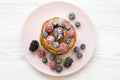 Pancakes with berries, honey and sugar on a pink plate over white wooden background, top view. Royalty Free Stock Photo