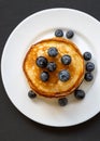 Pancakes with blueberries and honey on a white plate on a black wooden background, overhead view. Flat lay, top view, from above Royalty Free Stock Photo