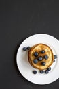 Pancakes with blueberries on a white round plate over black wooden background, top view. Copy space. Flat lay, overhead, from abov Royalty Free Stock Photo