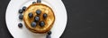 Pancakes with blueberries on a white round plate over dark background, top view. Copy space. Flat lay, overhead Royalty Free Stock Photo