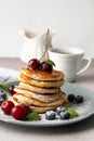 Pancakes with cherries, honey and blueberries, in the background a cup of coffee