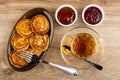 Pancakes from cottage cheese in brown dish, bowls with raspberry jam, apricot jam, fork, cup with tea, spoon on saucer on table. Royalty Free Stock Photo