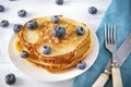 Pancakes with fresh blueberries on a plate, fork, knife on a blue napkin on a white wooden , top view Royalty Free Stock Photo