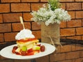 Pancakes with fresh fruits and whipped cream, and decorated artificial flowers in flowerpot on glass table with red brick wall ba Royalty Free Stock Photo