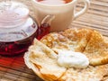 Hot pancakes on a plate with sour cream, a cup with red tea and a glass teapot Royalty Free Stock Photo