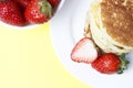 Pancakes on a plate and strawberries on a yellow background, top view