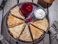 Pancakes rolled up in a big gray plate with a triangle, near a small ice-cream pan with sour cream and canned cherries Royalty Free Stock Photo