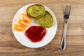 Pancakes with spinach, jam, slice of tangerine in plate, fork on wooden table. Top view