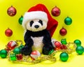 Panda Bear plush toy with Red Christmas Santa Hat surrounded by Tinsel Garland and Vintage Ornaments on bright yellow Royalty Free Stock Photo