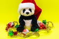 Panda Bear plush toy with Red Christmas Santa Hat surrounded by Tinsel Garland and Vintage Ornaments on bright yellow Royalty Free Stock Photo