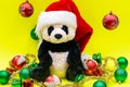 Panda Bear plush toy with Red Christmas Santa Hat surrounded by Tinsel Garland and Vintage Ornaments on bright yellow Royalty Free Stock Photo