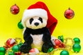 Panda Bear plush toy with Red Christmas Santa Hat surrounded by Tinsel Garland and Vintage Ornaments on bright yellow Royalty Free Stock Photo