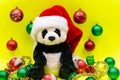 Panda Bear plush toy with Red Christmas Santa Hat surrounded by Tinsel Garland and Vintage Ornaments on bright yellow Royalty Free Stock Photo