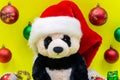 Panda Bear plush toy with Red Christmas Santa Hat surrounded by Tinsel Garland and Vintage Ornaments on bright yellow Royalty Free Stock Photo