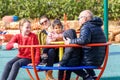 Happy family riding a carousel, spinning in a metal roundabout equipment at a playground on a sunny autumn day.