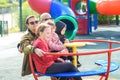 Happy family riding a carousel, spinning in a metal roundabout equipment at a playground on a sunny autumn day.