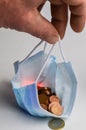 The pandemic purse - Human fingers hold a protective mask full of euro cents, concept to demonstrate the economic impoverishment Royalty Free Stock Photo