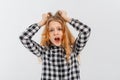 Panicking freaked out teen girl wearing casual plaid shirt screaming shocked and scared holding hands on head popping eyes at Royalty Free Stock Photo