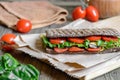 Panini - sandwich with brown bread, tomatoes, letuce and sausages on woodan background