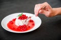 Panna cotta with currant syrup in white plate and hand with spoon on a dark background and berries. Traditional italian dessert.