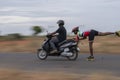 Panning shot of a man driving scooter and aboy holding and skating behind